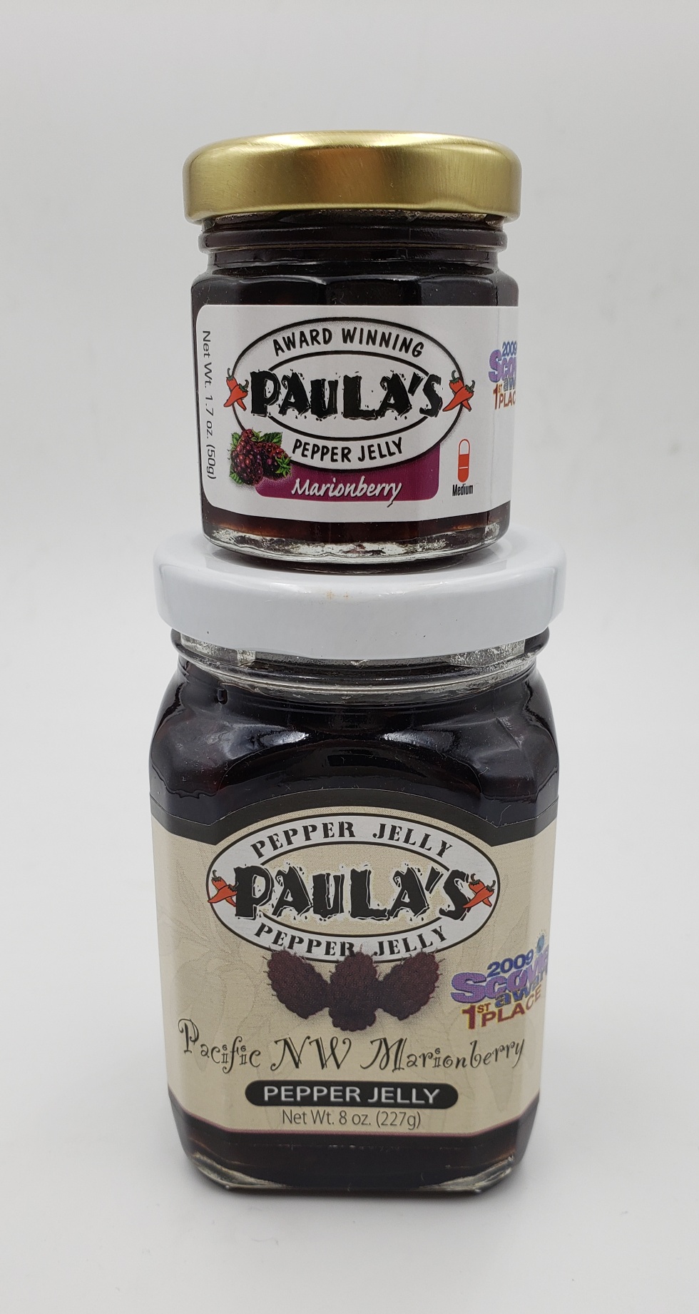 The 1.7 oz. marionberry pepper jelly jar on top of the 8 oz. Paula’s Pepper Jelly jar both full of marionberry pepper jelly.