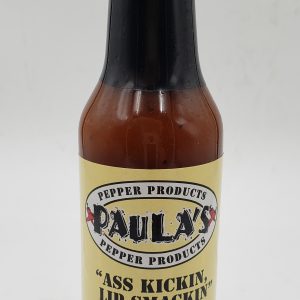Close-up of Paula’s organic hot sauce at Paula’s Pepper Jelly label side out. The label reads, “Paula’s Ass Kickin Lip Smackin Hot Sauce.”