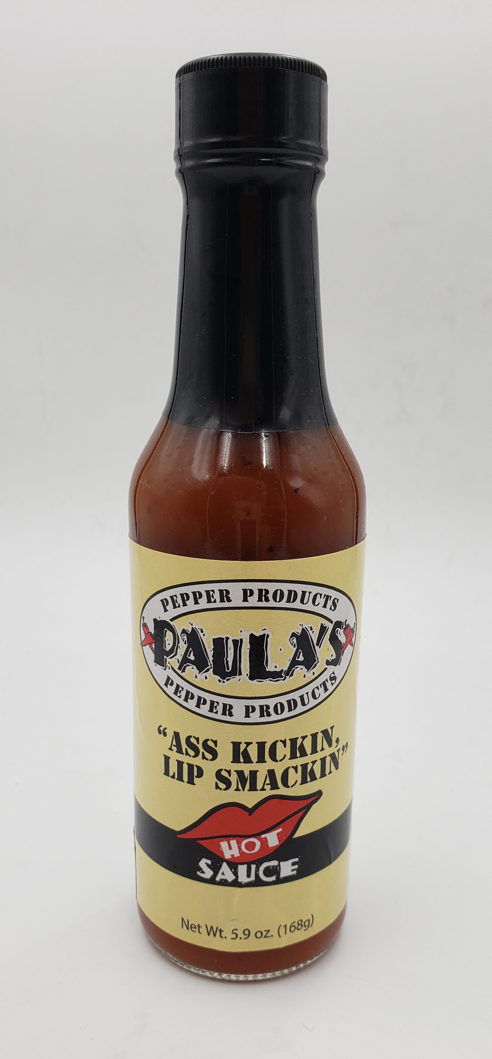 Close-up of Paula’s organic hot sauce at Paula’s Pepper Jelly label side out. The label reads, “Paula’s Ass Kickin Lip Smackin Hot Sauce.”