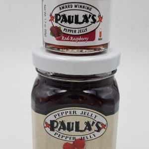 1.7 oz. Paula’s Pepper Jelly jar on top of the 8 oz. Paula’s Red Raspberry Pepper Jelly jar. Both are label out and full of pepper jelly.